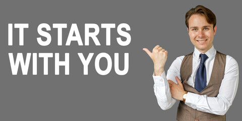Emotional portrait of businessman showing right hand gesture on text - IT STARTS WITH YOU. Gray background.