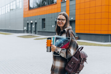 Fototapeta na wymiar portrait of young happy student holding books coffee smiling after passing exams. Smart woman on university campus. College life. Teenanger in braces, eyeglasses with bag back to school. College life.