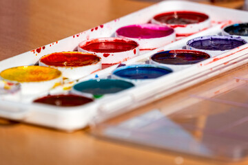 Old used box with watercolor multicolored paints on a wooden table