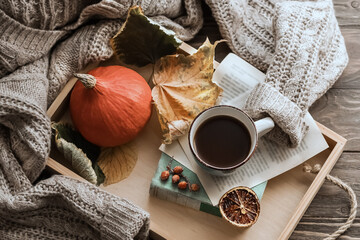 Autumn morning coffee. A cup of coffee on a wooden tray, a warm sweater in a book on a background of autumn leaves. Still life concept. Flat lay
