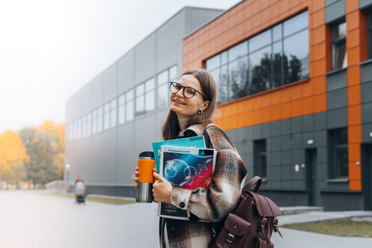 millennial caucasian female student in glasses and dental braces with books walking on campus after exam, lunch break. young smiling happy woman with backpack studying in college. University lifestyle