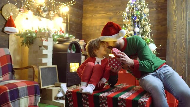 Father and son with magic gift at home near Christmas tree and fireplace. Dad and child hold Xmas prasent at home. Kid with parent giving presents and enjoy New Year.