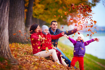 Fototapeta premium happy family playing among fallen leaves in autumn park
