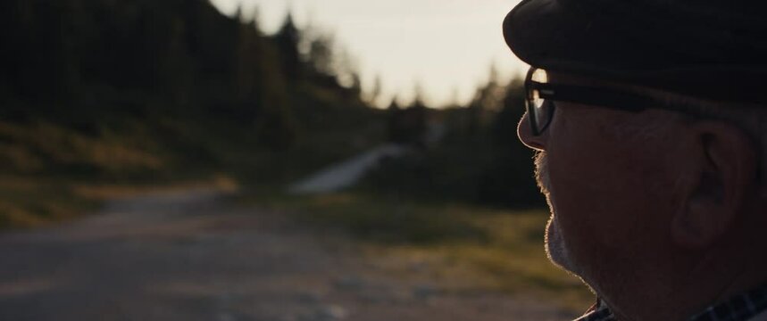 Senior mountain farmer man glasses hat thinking in Alps mountain sunrise