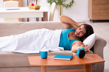 Young man lying on the sofa in time management concept