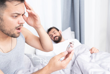 Fototapeta premium Worried young man being late for work with boyfriend sleeping in bed