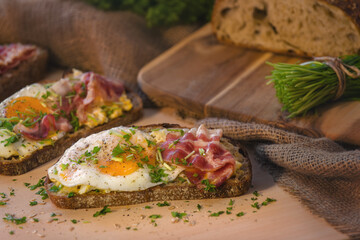 Brunch in the form of oatmeal sourdough bread garnished with fried egg, bacon, chives and parsley. Decorated with jute fabric.