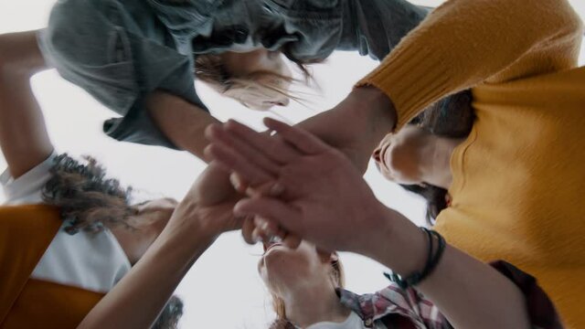 Group of friends joining and lifting hands into the air. Four women having fun outdoors on a weekend.
