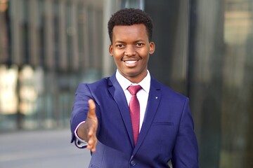 Positive man, businessman in formal suit suggest, giving hand, palm for business handshaking, greeting. Young black African Afro American guy with open hand looking at camera, smile. Welcome