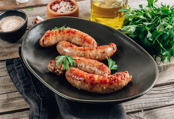 Grilled sausage with greens on black plate over rustic wooden background.