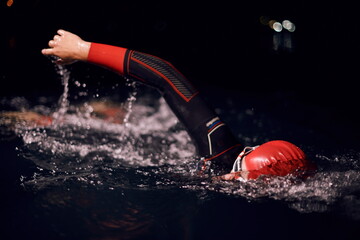 triathlon athlete swimming in dark night wearing wetsuit