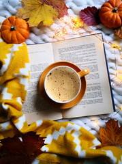 Autumnal composition with open book, coffee cup, rusty leaves, pumpkins and yellow blanket on white knitted throw. Top view, from above, flat lay. Relaxing at home and hygge concept.