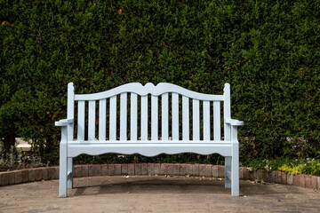緑の生垣の前に置かれた白いベンチ