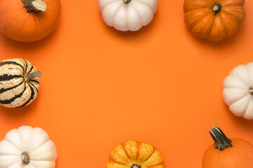 Colored pumpkins on orange background with place for text in the middle. Halloween flat lay composition.