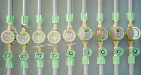 Row of industrial pipelines and valves with green wheels on  grey wall.