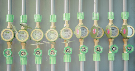 Fototapeta premium Row of industrial pipelines and valves with green wheels on grey wall.