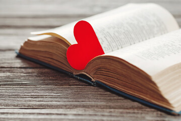 open book with red heart shaped paper bookmark on wooden background