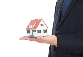 Fototapeta na wymiar A house salesperson in a black suit and blue tie holds a small house model