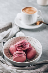 Several small macaroon cakes in a plate for breakfast and a cup of coffee on the table, vertical photo