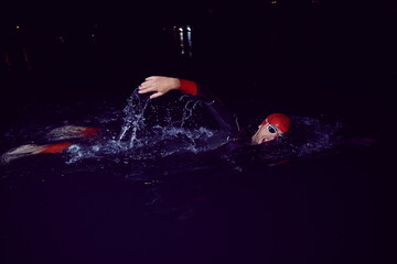 triathlon athlete swimming in dark night wearing wetsuit