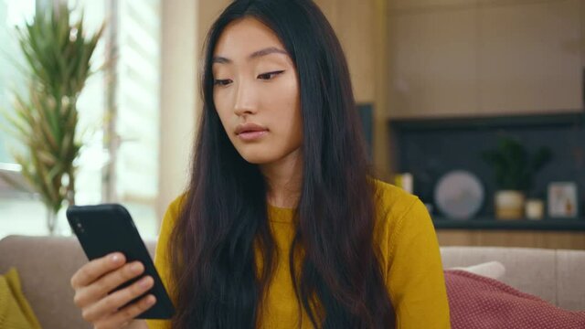 Cute asian young woman use phone sitting on sofa at home. Social media text email enjoy distant communication. Social media. Close up. Slow motion