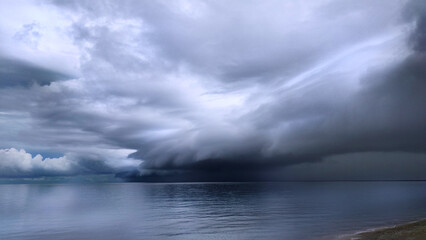 Dark storm clouds gather over Surigao Strait near Mabua Beach in the Philippines, showing calm coastal waters beneath an overcast sky and changing weather conditions along the shoreline.
