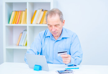 Senior man at laptop paying with credit card for online shopping