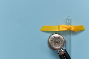 A round stethoscope membrane next to an empty inverted glass test tube with a yellow bow made of satin ribbon braid.
