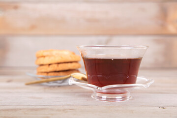 A bowl of hot black tea and a plate of refreshments on a wooden background