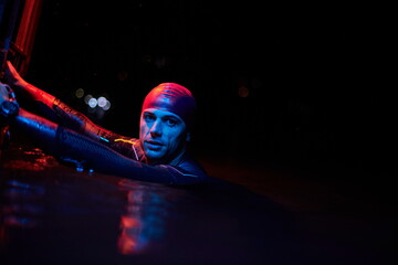 authentic triathlete swimmer having a break during hard training on night neon gel light