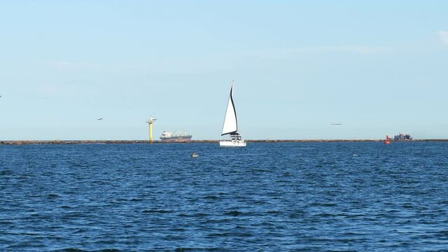 Beautiful white sailboat sails in from the Gulf of Mexico near Port Aransas, on the blue water of the ship channel to Corpus Christi, Texas. Subtle zoom in.