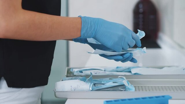 Female professional dentist preparing wrapped packages with dental instruments after autoclave sterilization process. Dental assistant. Stomatology.