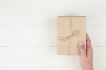 Hand of man holding gift giving on wooden table in Christmas day or holiday, present box for anniversary or birthday or celebration with copy space, celebrate and festive, top view, flat lay.