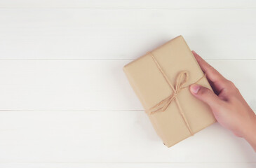 Hand of man holding gift giving on wooden table in Christmas day or holiday, present box for anniversary or birthday or celebration with copy space, celebrate and festive, top view, flat lay.