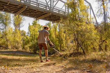 Prospector man uses a metal detector to look for lost gold treasure from the Walnut Grove Dam disaster under the Hassayampa River Bridge outside Kirkland, Arizona, USA in autumn
