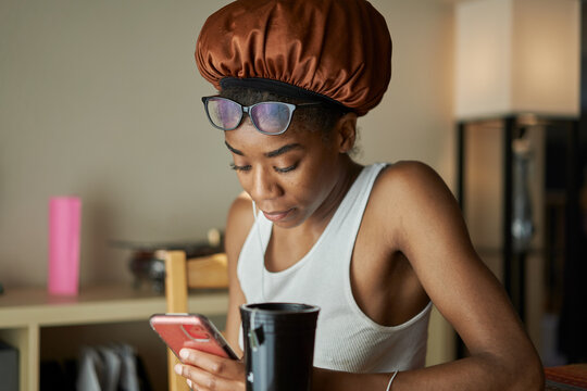 african american woman wearing showercap looking at smartphone during morning routine