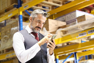 Senior store manager in formal wear using mobile phone to tracking shipment online while checking inventory in distribution warehouse 