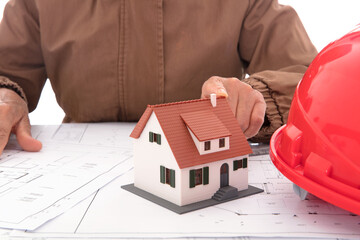 The architect points his finger at the house model on the blueprint