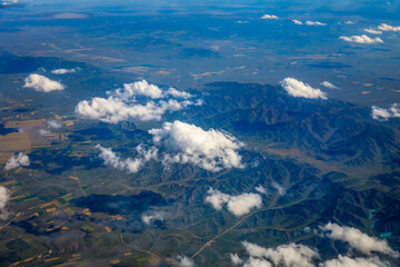Naklejka na ściany i meble Aerial view above the clouds and mountain peaks on a sunny day.mountain view from airplane.