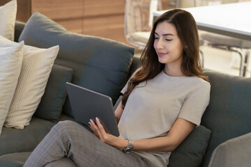 Beautiful woman relax sitting on couch and using digital tablet browsing on the internet, chatting with friend or watching movie in living room at home at night. concept for social media communication