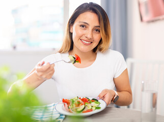 Portrait of positive latino woman tasting fresh green salad with pleasure at home