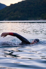 triathlon athlete swimming on lake in sunrise wearing wetsuit