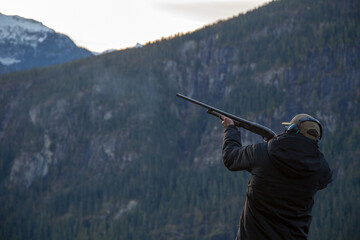 A man holds a shotgun downrange ready to fire at a clay pigeon to practice his aim in Squamish,...