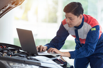  Asian technician or Auto mechanic check engine system. new car with a notebook computer in car service center.
