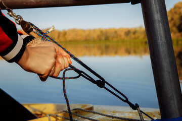 A man's hands tie a sea knot on a light yacht. the ropes holding the mast of the ship. In the background, a lake and an autumn forest.