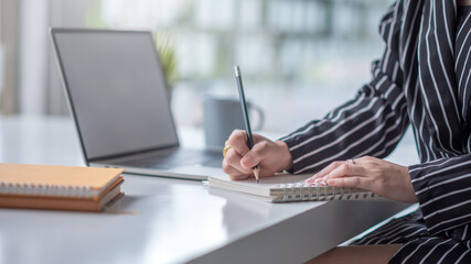 Businesswoman working on laptop and taking note while sitting at the table in office.