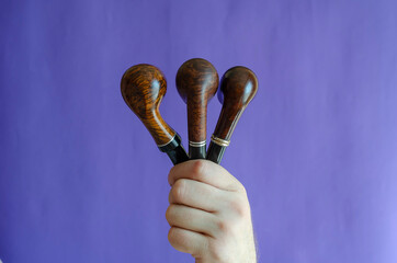 A male hand holds three smoking pipes on a blue background.