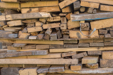 Stacked as a woodpile are many wooden yellow gray boards, planks, and slats of various sizes and cross-sections.