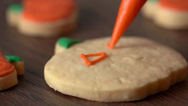 Close up of decorating cute Halloween pumpkin gingerbread cookies with frosting icing cream topping bag.