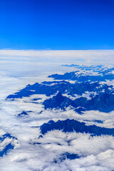 Obraz premium Aerial view above the clouds and mountain peaks on a sunny day.